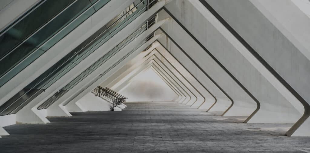 Passage moderne avec arches blanches et plafond vitré, créant une perspective triangulaire sur un sol pavé.